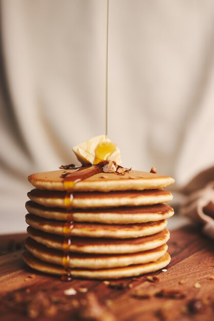 Vertical shot of pancakes with syrup, butter and roasted nuts on a wooden plate