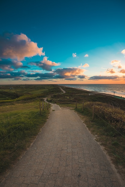 Vertical shot of a paved pathway by the sea under the cloudy sky captured in Domburg, Netherlands