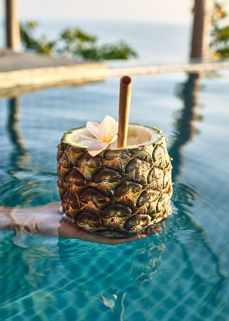 無料Photo プールでパイナップルの飲み物を持っている人の垂直ショット