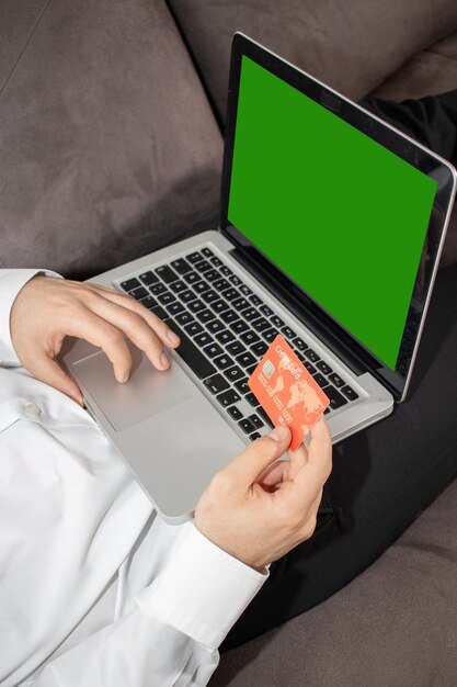 Вертикальный снимок человека, вводящего данные своей кредитной карты в ноутбук