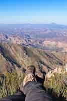 Foto gratuita colpo verticale dei piedi di una persona seduta in cima a una collina sopra una bellissima valle