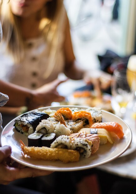 Vertical shot of a person's hand holding a plate of sushis