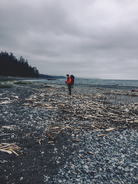 Vertical shot of a person standing on a rocky beach next to the ocean