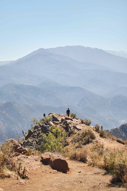 Vertical shot of a person walking back from the edge of a mountain in the distance