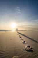 Free photo vertical shot of a person walking on the sandy beach with footsteps on the foreground