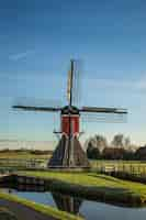 Free photo vertical shot of a post mill on a grassy field with wooden fences and a blue sky