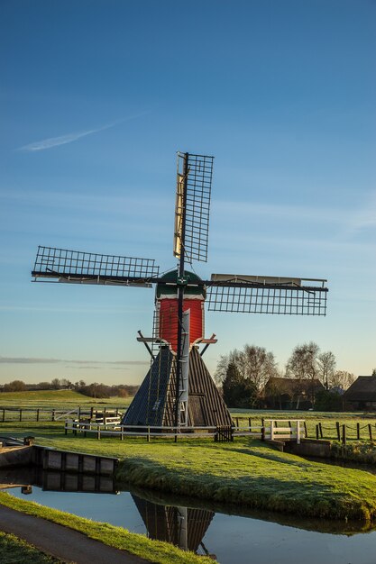 Vertical shot of a post mill on a grassy field with wooden fences and a blue sky