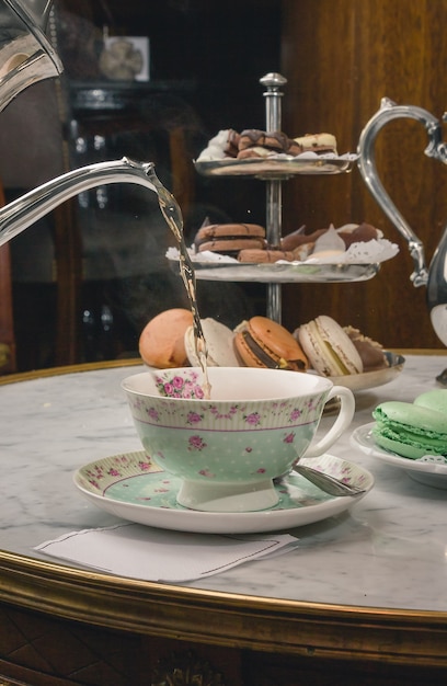 Free photo vertical shot of a pouring tea in a cup on a marble table with desserts