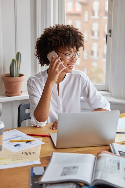 Vertical shot of pretty black businesswoman examines charts on papers