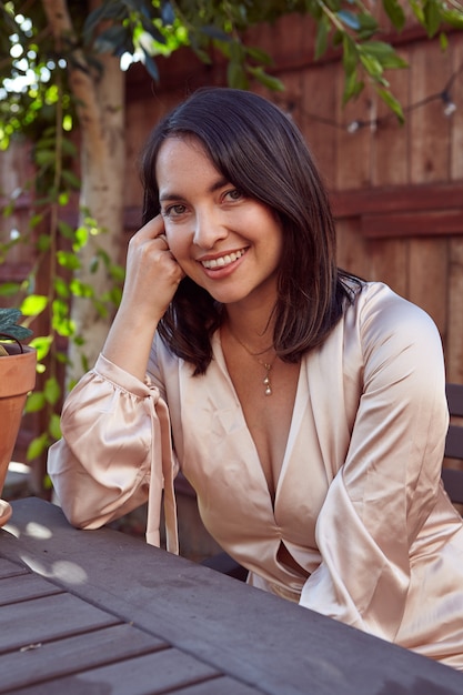 Vertical shot of a pretty female with a pink silk dress sitting in an outdoor cafe