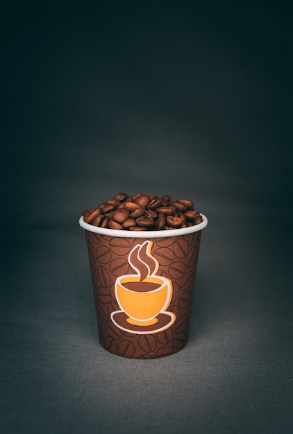 어두운 벽에 고립 된 볶은 커피 콩의 전체 인쇄 컵의 세로 샷