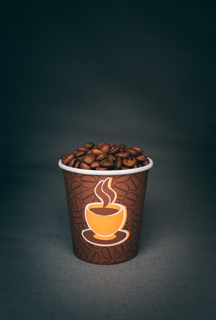 Vertical shot of a printed cup full of roasted coffee beans isolated on dark wall