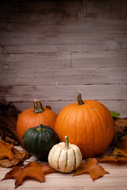 Vertical shot of pumpkins surrounded by leaves with a wooden background for Halloween