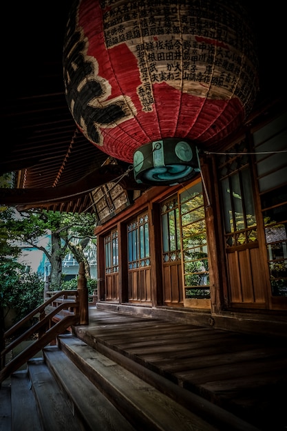 Vertical shot of red lantern over the stairs near the wooden Japanese style house