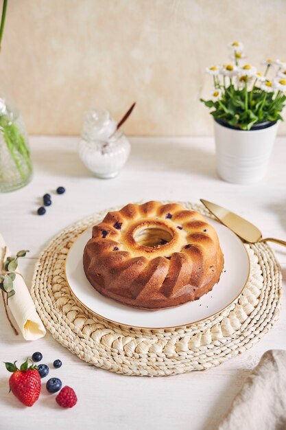 Vertical shot of a ring cake with fruits on a white table with white surface