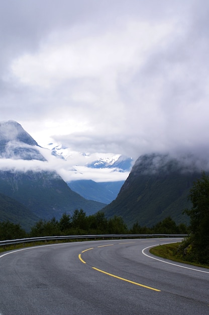 Vertical shot of a road surrounded by high rocky mountains covered with white clouds