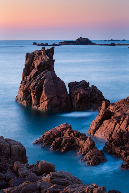 Vertical shot of rock formations in the beautiful clear blue sea in Guernsey
