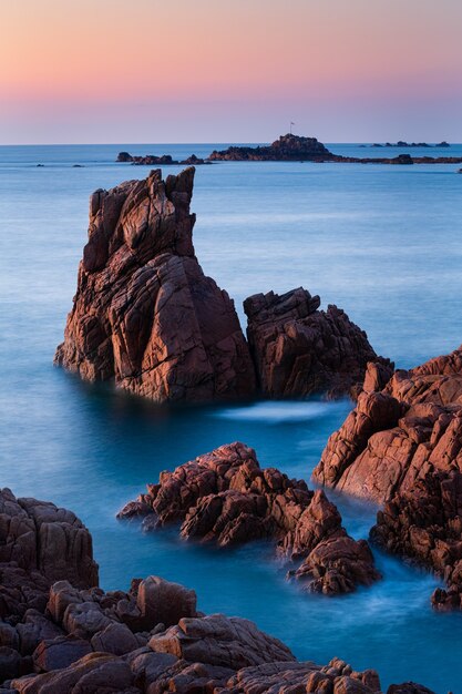 Vertical shot of rock formations in the beautiful clear blue sea in Guernsey