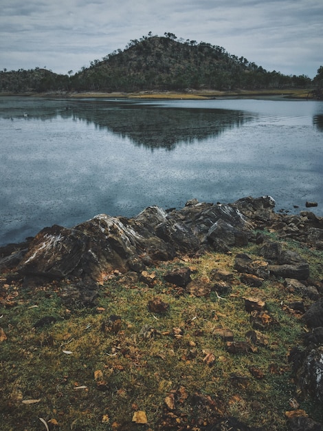 Vertical shot of rocks near the water reflecting the mountain