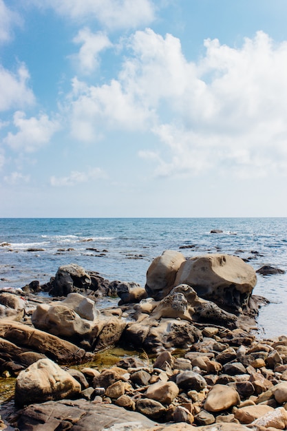 Vertical shot of rocks at the seashore under the cloudy sky