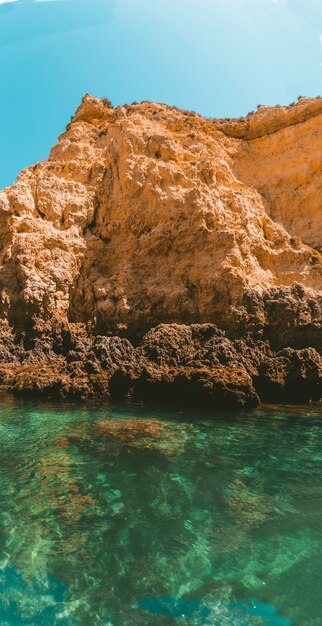 Vertical shot of a rocky cliff reflecting on the sea on a sunny day