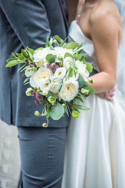 Vertical shot of a romantic groom and bride holding a bridal bouquet