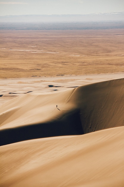 Vertical shot of sand dunes and a dry field in the distance