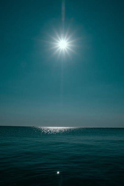 Vertical shot of a sea reflecting the sun with clear blue sky