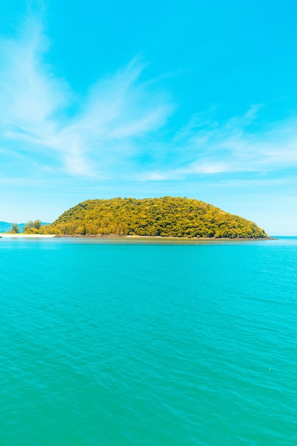 Vertical shot of the sea with an island covered in trees under a blue sky