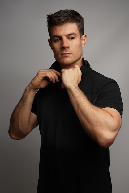 Vertical shot of a sexy male adjusting collar while standing against a gray wall