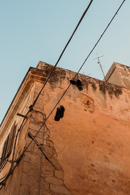 Vertical shot of shoes handing from an electric cable near a building under a blue sky