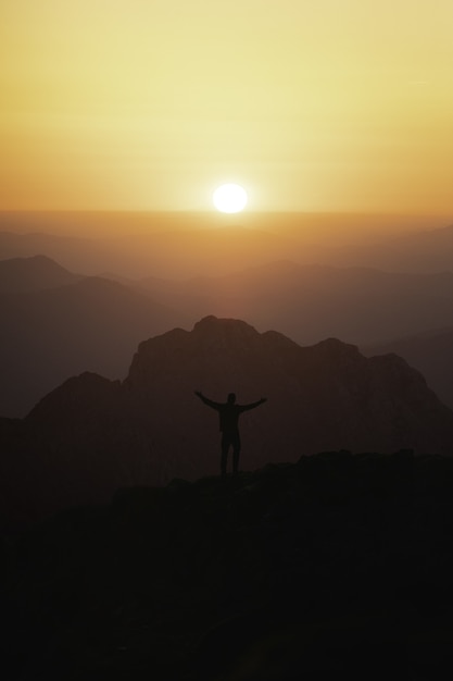 夕日を見ている山の頂上で男性観光客のシルエットの垂直ショット