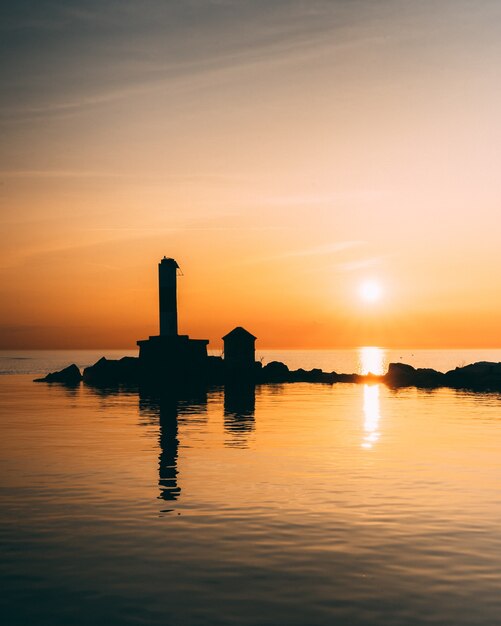 Vertical shot of silhouettes of the buildings in the middle of a calm ocean during sunset