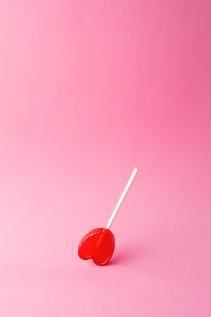 Vertical shot of a single heart-shaped lollipop on a pink background