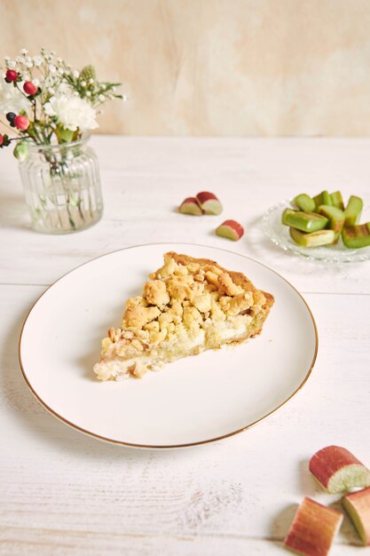 Vertical shot of a slice of crispy Rhabarbar cake tart and some ingredients on a white plate