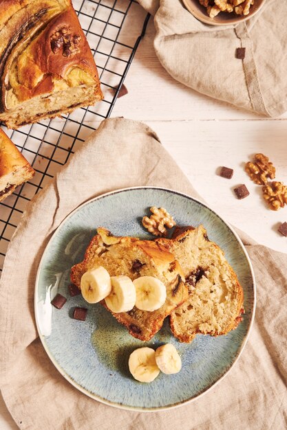 Вертикальный снимок ломтиков вкусного бананового хлеба с кусочками шоколада и грецкими орехами на тарелке