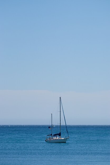 Vertical shot of a small boat sailing in the ocean with a clear blue sky