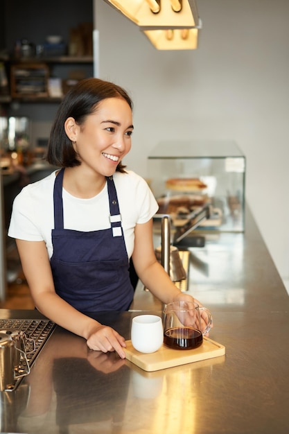Vertical shot of smiling asian barista girl working in cafe giving order to client made batch brew f