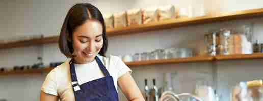 Free photo vertical shot of smiling asian girl putting coffee in tamper to brew capuccino prepare order in