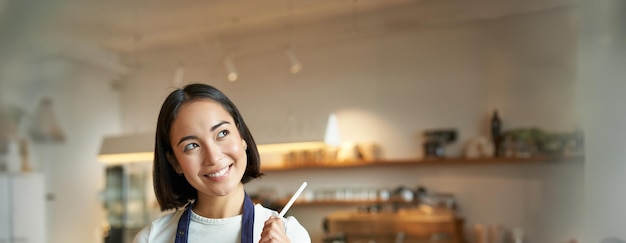 Free photo vertical shot of smiling girl waitress barista in coffee shop wears blue apron uniform takes order