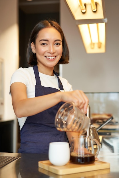 Free photo vertical shot of smiling korean barista pouring filter coffee prepare batch brew for client in cafe pour over method