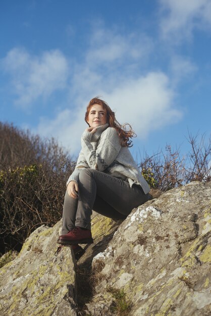 Vertical shot of a smiling woman sitting on the shore with the trees