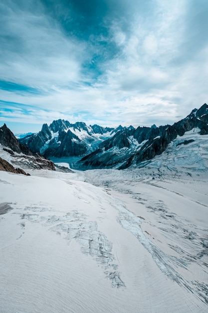 Free photo vertical shot of a snowy hill with mountains in the distance under a cloudy sky