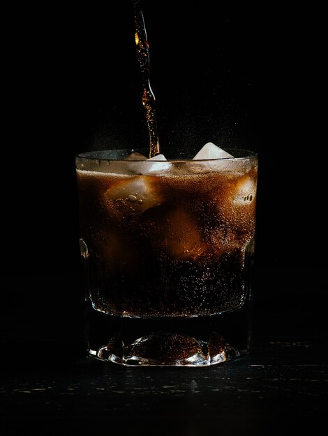 Vertical shot of soda being poured in a glass full of ice