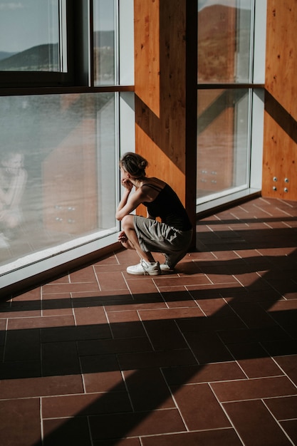 Vertical shot of a squatting female looking out of the window