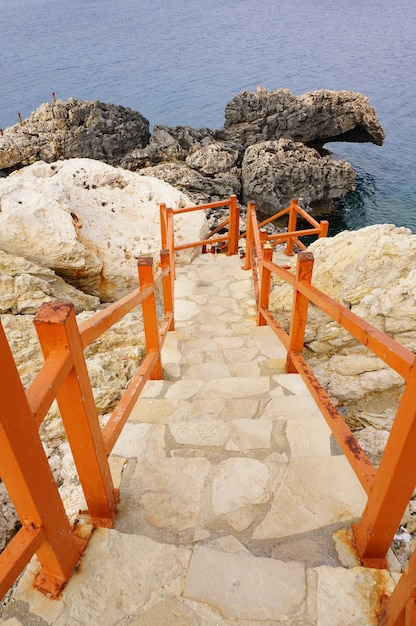 Free photo vertical shot of the stairs with a wooden fence surrounded by rocks and stones near the ocean