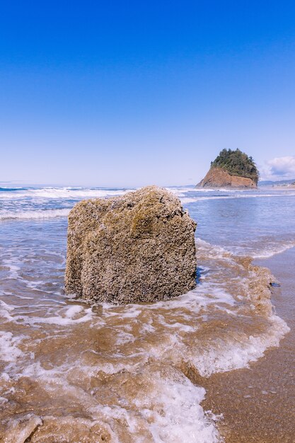 Vertical shot of a stone in the ocean under the blue clear sky