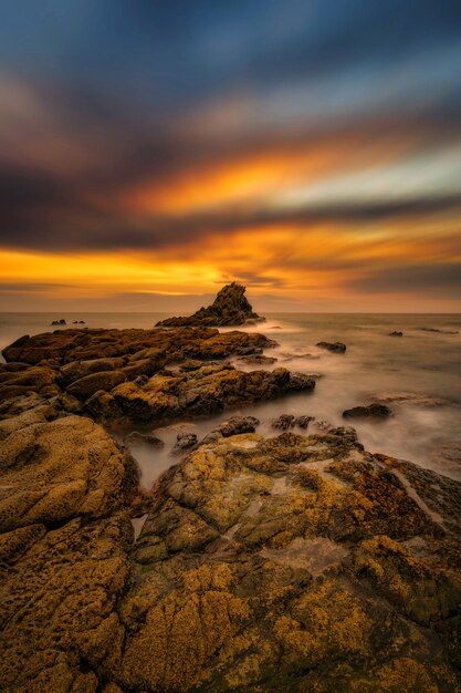 Вертикальный снимок камней на берегу моря под фантастическим восходом солнца