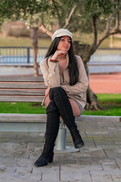 Вертикальный снимок стильной кавказской женщины, сидящей на скамейке и позирующей