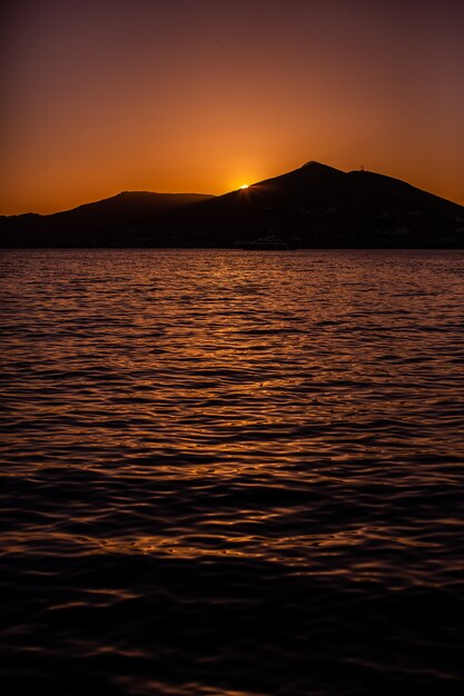 Vertical shot of the sun setting behind a mountain in Naxos, Greece